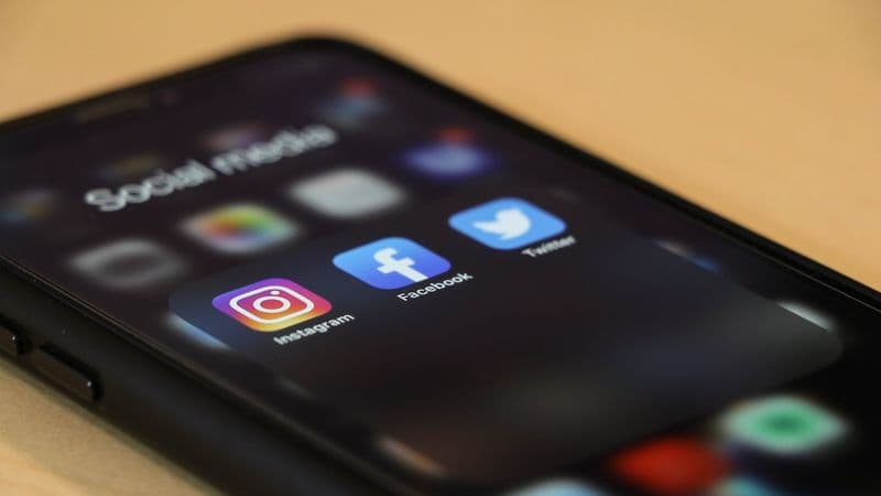 Smartphone displaying social media app icons on a wooden desk